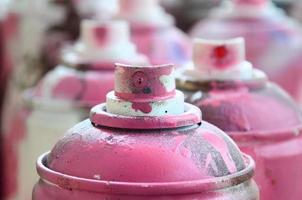 A lot of dirty and used aerosol cans of bright pink paint. Macro photograph with shallow depth of field. Selective focus on the spray nozzle photo
