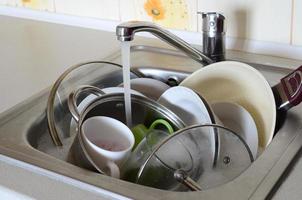 Dirty dishes and unwashed kitchen appliances lie in foam water under a tap from a kitchen faucet photo