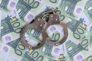 Police handcuffs lies on a set of green monetary denominations of 100 euros. A lot of money forms an infinite heap photo