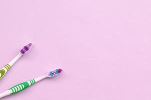 Two toothbrushes lie on a pastel pink background photo