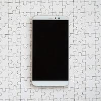 A modern big smartphone with a touch screen lies on a white jigsaw puzzle in an assembled state photo