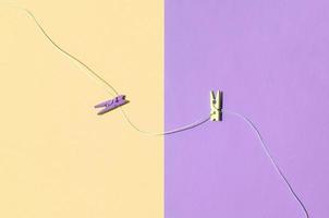 Two colored wooden pegs and small rope lie on texture background of fashion pastel yellow and violet colors photo