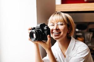 Excited blonde girl taking photos. Laughing photographer in glasses holding camera. photo