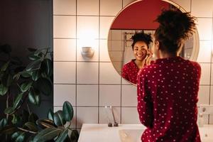 Girl in polka-dot pajamas with smile looks in mirror and touches her skin on her face. photo