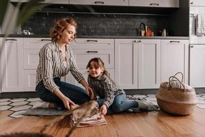 mujer pelirroja rizada y su hermosa hija se sientan en la alfombra en la cocina y charlan foto