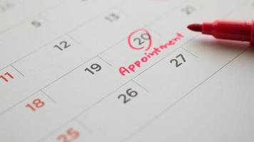 Red color marker pen pointing at important appointment schedule on white calendar page date close up photo