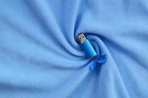 Brilliant blue usb flash memory card with a blue bow lies on a blanket of soft and furry light blue fleece fabric with a lot of relief folds. Memory storage device in women's design photo