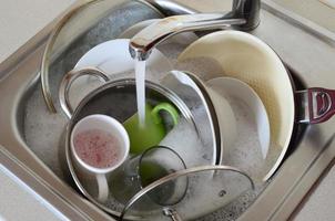 Dirty dishes and unwashed kitchen appliances lie in foam water under a tap from a kitchen faucet photo