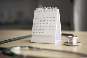estetoscopio con fecha de página de calendario en el fondo de la mesa de madera concepto médico de cita médica foto