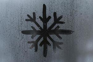 The image of the snowflake is drawn with a finger on the surface of a misted glass window. Frosty weather photo