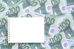 cuaderno blanco con páginas limpias sobre un conjunto de denominaciones monetarias verdes de 100 euros. mucho dinero forma un montón infinito foto