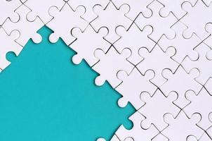 Fragment of a folded white jigsaw puzzle on the background of a blue plastic surface. Texture photo with copy space for text