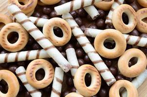 A lot of crispy sweet tubules, chocolate melting balls and yellow bagels lie on a wooden surface. Close up view photo