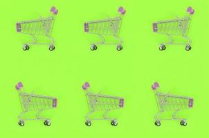 Shopping addiction, shopping lover or shopaholic concept. Many small empty shopping carts perform a pattern on a pastel colored paper background. Flat lay composition, top view photo