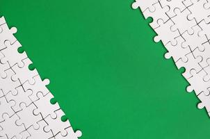 Fragment of a folded white jigsaw puzzle on the background of a green plastic surface. Texture photo with copy space for text