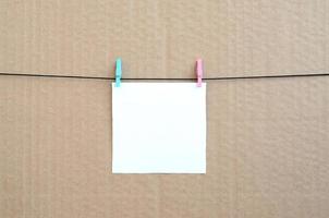 White blank card on rope on a brown cardboard background. Creative reminder, small sheet of paper on wooden clothespin, memo backdrop photo