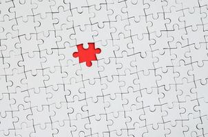 The texture of a white jigsaw puzzle in an assembled state with one missing element forming a red space photo