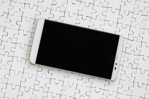 A modern big smartphone with a touch screen lies on a white jigsaw puzzle in an assembled state photo