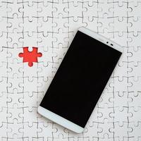 A modern big smartphone with a touch screen lies on a white puzzle puzzle in an assembled state photo