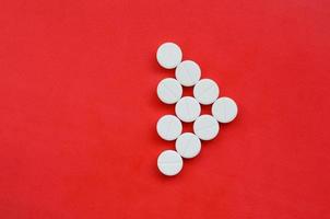 Several white tablets lie on a bright red background in the form of a triangular arrow. Background image on medicine and pharmaceutical topics photo