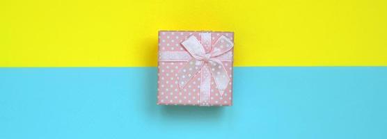 Small pink gift box lie on texture background of fashion pastel blue and yellow colors paper in minimal concept photo