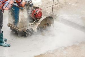 Worker using diamond saw blade machine cutting concrete road at construction site photo