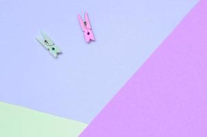 Two colored wooden pegs lie on texture background of fashion pastel violet, turquoise and pink colors paper photo