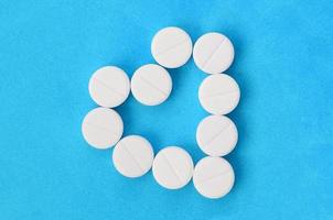 Several white tablets lie on a bright blue background in the shape of a heart. Background image on medicine and pharmaceutical topics photo