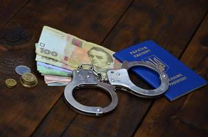 A photograph of a Ukrainian foreign passport, a certain amount of Ukrainian money and police handcuffs. The concept of arresting Ukrainian illegal immigrants while trying to bribe photo