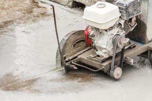 trabajador que utiliza una máquina de hoja de sierra de diamante cortando una carretera de hormigón en el sitio de construcción foto