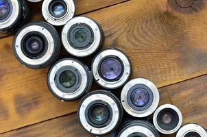 Several photographic lenses lie on a brown wooden background. Space for text photo