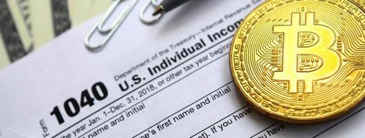 The pen, bitcoins and dollar bills is lies on the tax form 1040 U.S. Individual Income Tax Return. The time to pay taxes photo