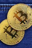 dos bitcoins dorados se encuentran en una tela de jeans azules. nuevo dinero virtual. nueva moneda criptográfica en forma de monedas foto