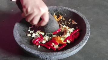 o processo de fazer um molho de pimenta. uma mão está pulverizando cebolas e pimentas em um pilão em um almofariz de pedra para fazer um molho de pimenta. video