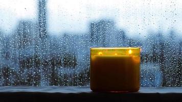 une bougie aromatique brûlante se place près d'une fenêtre qui a des gouttes de pluie pendant la saison de la mousson. concept zen et relaxant.