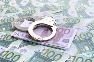 Police handcuffs lies on a set of green monetary denominations of 100 euros. A lot of money forms an infinite heap photo