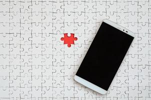 A modern big smartphone with a touch screen lies on a white puzzle puzzle in an assembled state photo