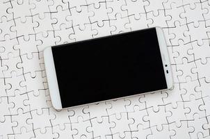 A modern big smartphone with a touch screen lies on a white jigsaw puzzle in an assembled state photo