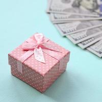 Pink dotted gift box lies near hundred dollar bills on a light blue background photo