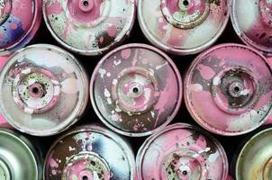 A few used spray cans with pink paint drips lie on texture background of fashion pastel pink color paper in minimal concept photo