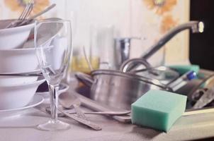 A huge pile of unwashed dishes in the kitchen sink and on the countertop photo