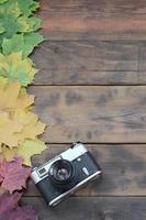 The old camera among a set of yellowing fallen autumn leaves on a background surface of natural wooden boards of dark brown color photo