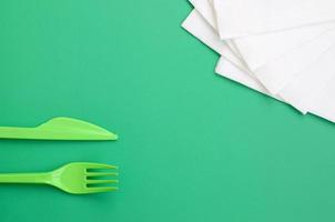 Disposable plastic cutlery green. Plastic fork and knife lie on a green background surface next to napkins photo