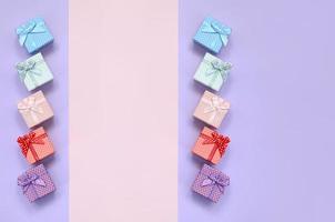 Small gift boxes of different colors with ribbons lies on a violet and pink color background photo