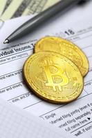 The pen, bitcoins and dollar bills is lies on the tax form 1040 U.S. Individual Income Tax Return. The time to pay taxes photo