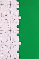 Fragment of a folded white jigsaw puzzle on the background of a green plastic surface. Texture photo with copy space for text