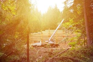 el proceso de construcción de una casa de madera a partir de vigas de madera de forma cilíndrica. grúa en condiciones de trabajo foto