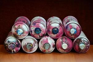 Bodegón con un gran número de latas de aerosol de colores usadas sobre la superficie de madera tratada en el taller de graffiti del artista. latas sucias y manchadas para spray art foto
