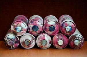 Still life with a large number of used colorful spray cans of aerosol paint lying on the treated wooden surface in the artist's graffiti workshop. Dirty and stained cans for spray art photo