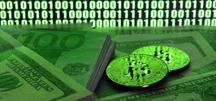 Two bitcoins lies on a pile of dollar bills on the background of a monitor depicting a binary code of bright green zeros and one units on a black background. Low key lighting photo